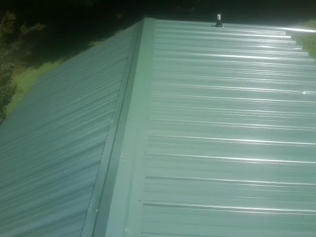 New green metal panels meeting at the ridge of a roof — Flat Roof Repair work by our crew in Atlantic Beach